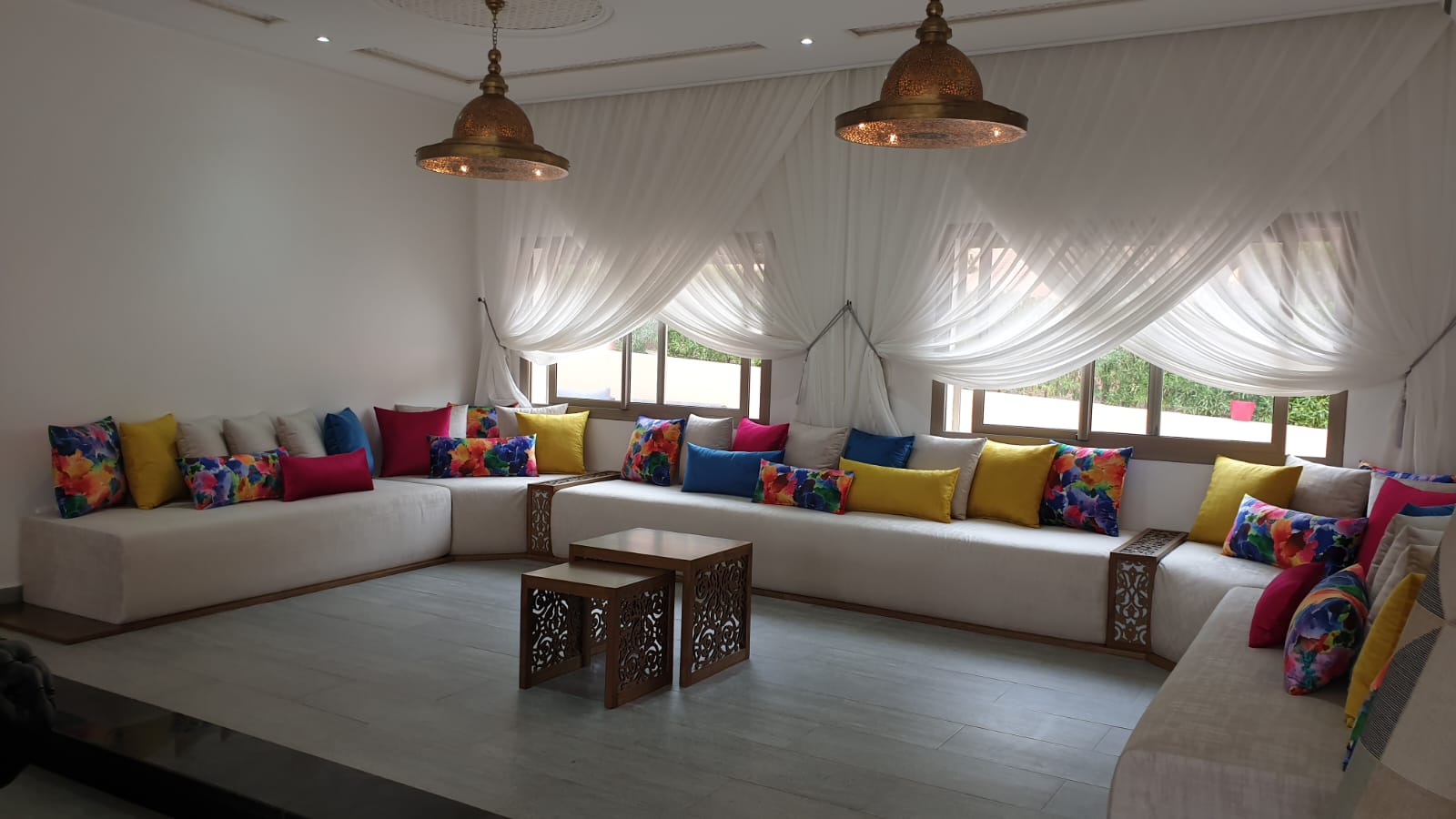 Vaste salon de réception marocain aux voilages blancs et lustres en laiton ajouré